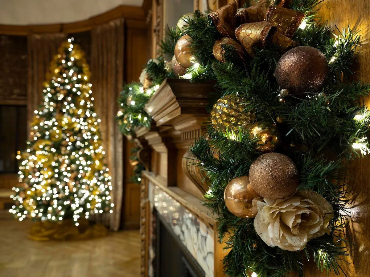 Gold bauble garland on a fireplace with a lit Christmas tree behind